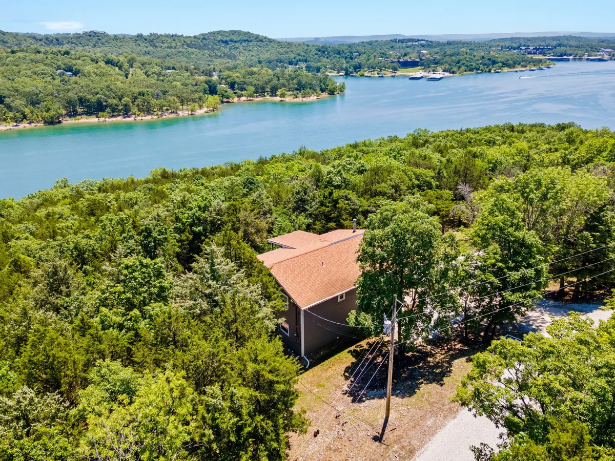 This image showcases the exterior of the property nestled among trees, with Table Rock Lake glimmering nearby. The tranquil mood is accentuated by a beautiful sunset, and you can see open spaces ideal for lakeside activities like fishing, boating, and picnicking.
