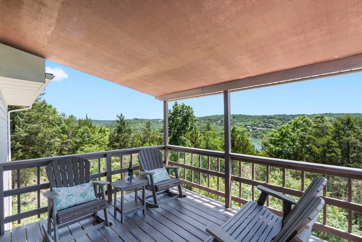 The image showcases a peaceful wooden deck furnished with comfortable chairs and a small table, overlooking a breathtaking landscape with sweeping views of Table Rock Lake. The tranquil setting is perfect for relaxing, sipping wine at sunset, or starting the day with a sunrise coffee, all while surrounded by nature. The expansive lake and wooded backdrop evoke a sense of privacy and connection to the outdoors.