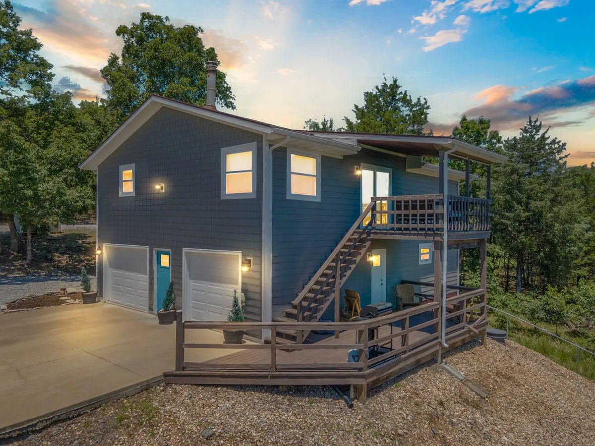 An inviting exterior shot of the house featuring the staircase leading up to the deck, surrounded by lush green trees. The scene conveys the sense of a welcoming launchpad for adventure and a peaceful retreat after a day of excitement.