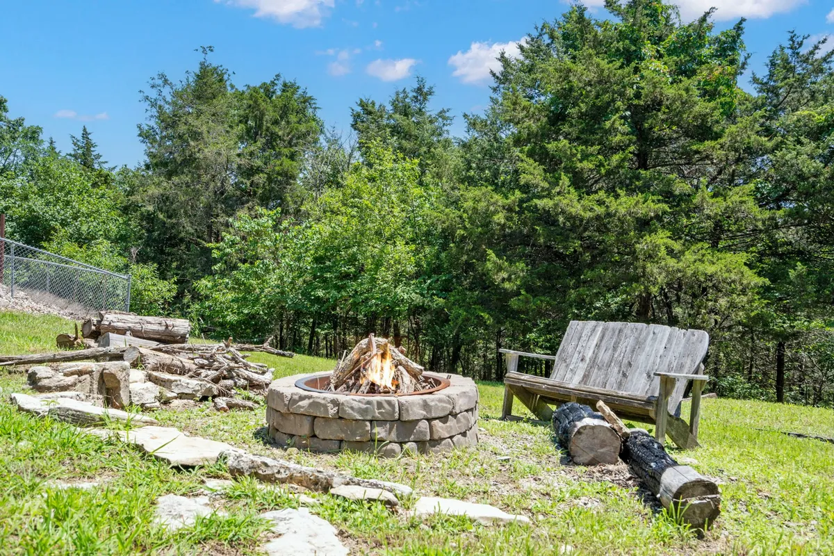 A cozy exterior setting featuring a fire pit surrounded by ample seating, nestled among trees. The scene evokes communal gatherings, storytelling, and stargazing under the open sky.