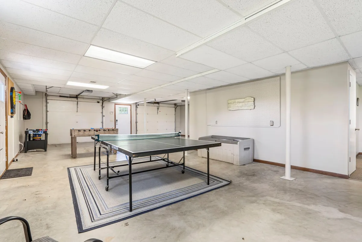 A garage interior with a ping pong table set up in the center, next to a workbench and large garage doors. The space feels open and casual, inviting guests to enjoy friendly matches or simply hang out together.