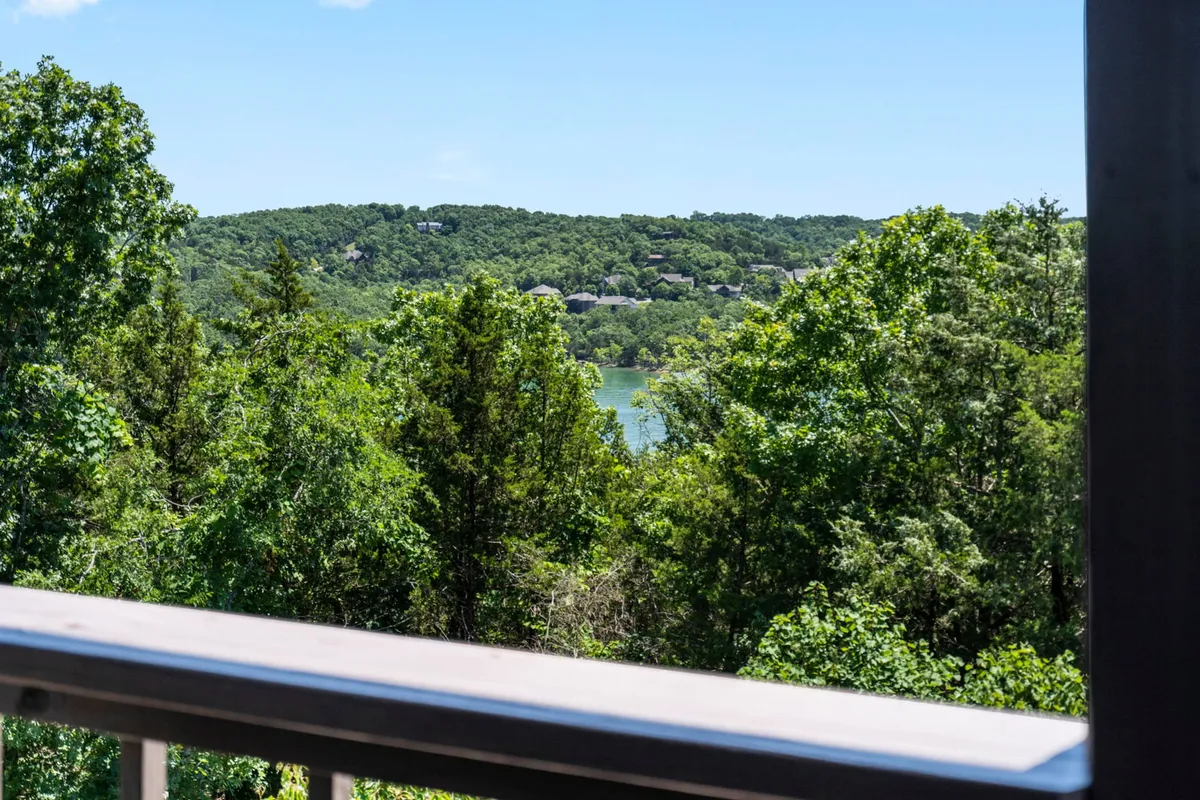 A panoramic vista of rolling green hills, dense tree cover, and a distant lake under a soft sky. The view provides a sense of peaceful seclusion and invites thoughts of exploring the outdoors, birdwatching, or simply soaking in the landscape.