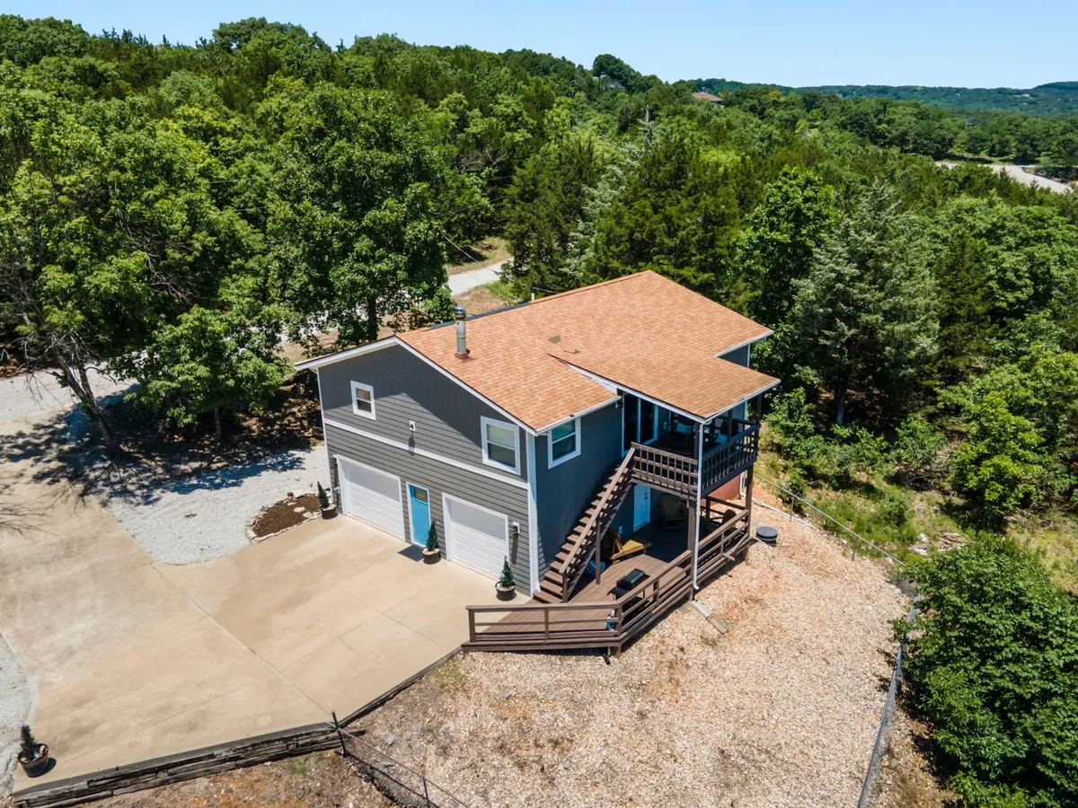 A peaceful exterior view of the house, highlighting the spacious deck surrounded by trees. The deck is positioned to capture beautiful sunset views and provide a comfortable vantage point, possibly even for watching nearby attractions like Silver Dollar City coasters in the distance.