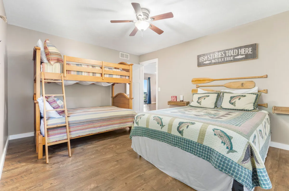 A spacious bedroom features both a plush queen bed and a twin-over-full bunk bed with playful, fishing-themed decor. The room feels both comfortable and lively, perfect for children and extra guests to unwind and bond after a busy day.