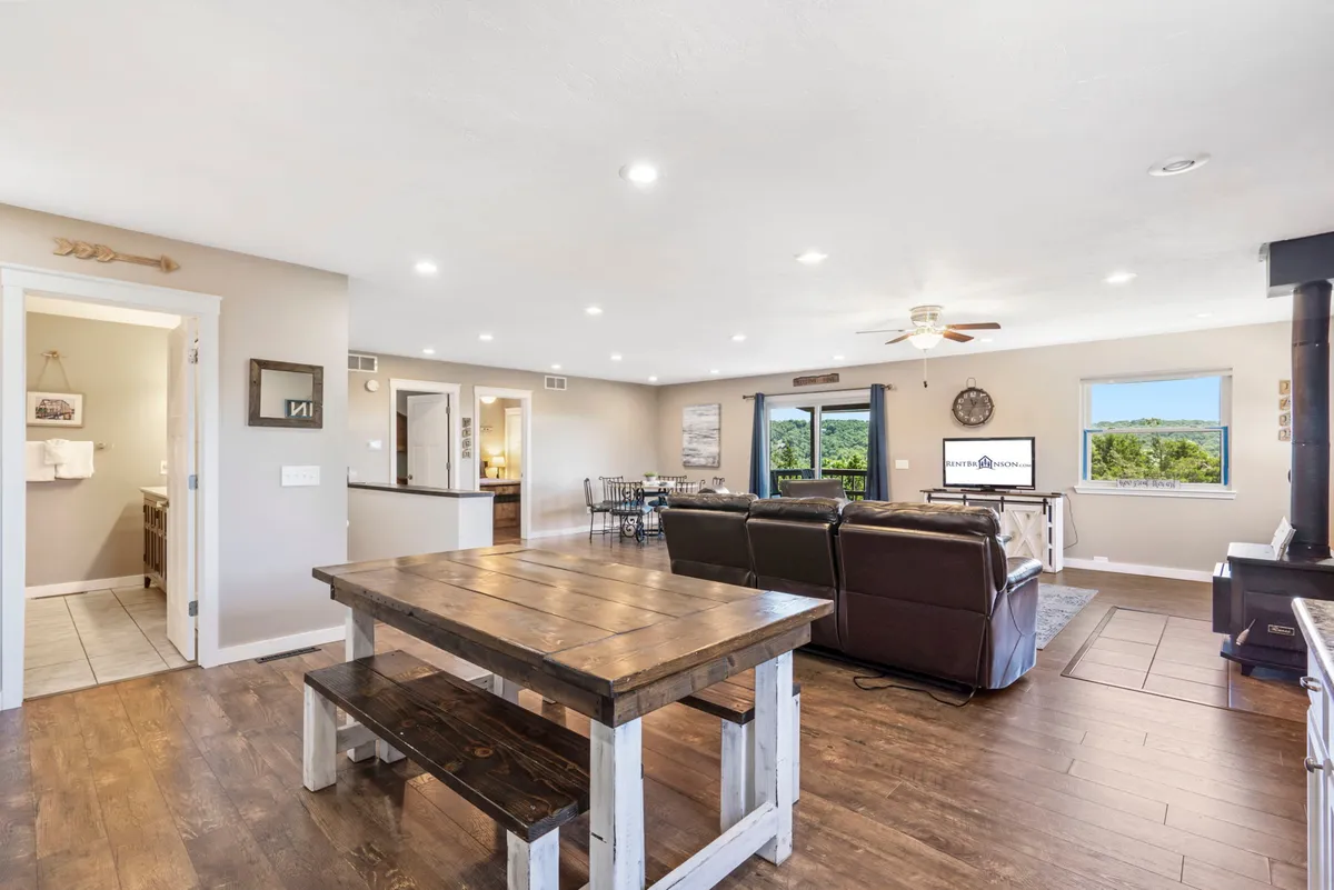 A cozy seating area with a dining table, comfortable chairs, a television, and large windows revealing views of nature. The arrangement invites guests to gather for meals, entertainment, and relaxation while staying visually connected to the outdoors.